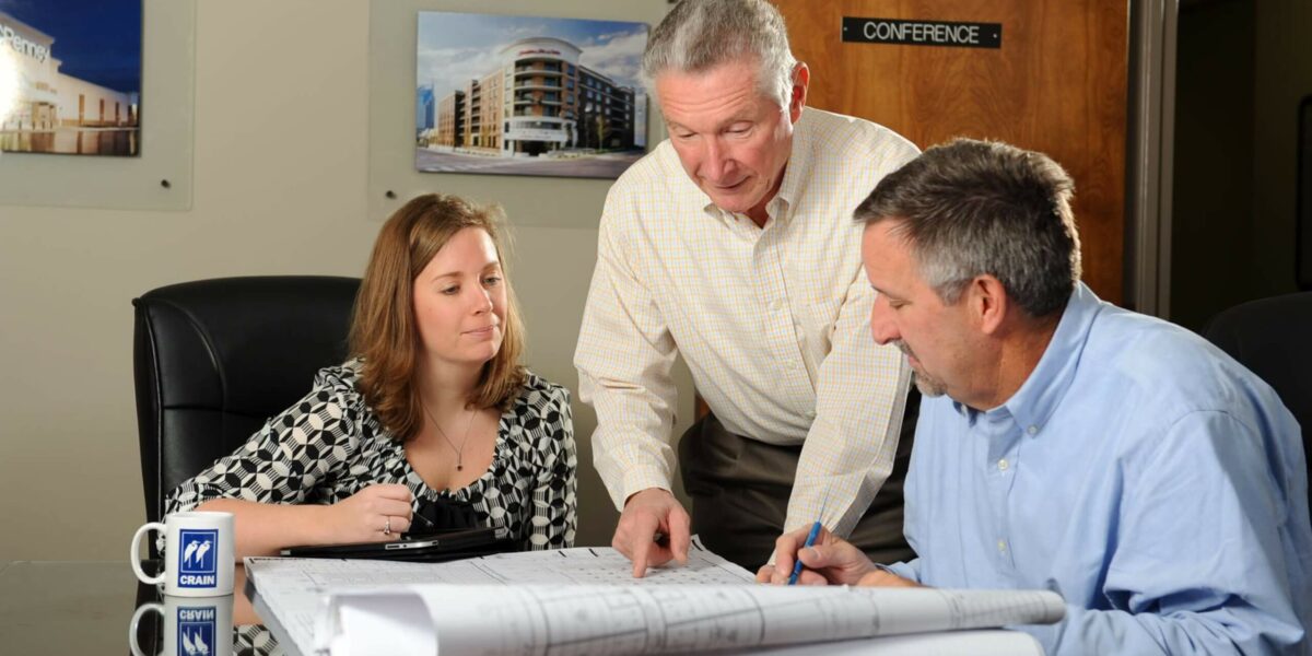 The Crain Construction team reviewing construction plans leaning over a in a conference room table.