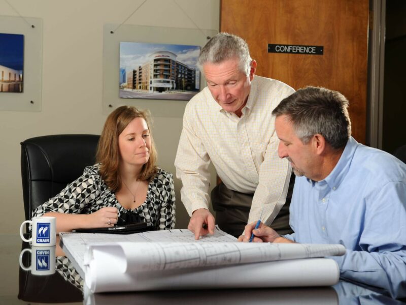 The Crain Construction team reviewing construction plans leaning over a in a conference room table.