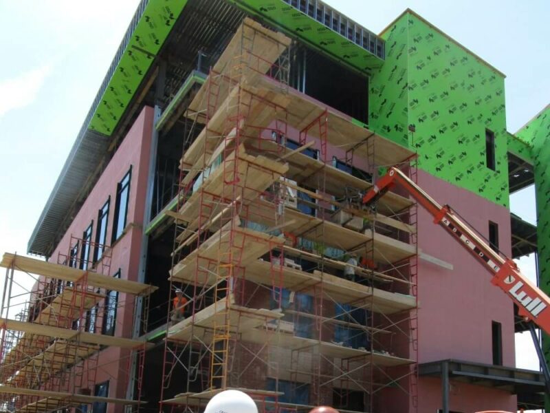 Two construction workers looking at a building that has been wrapped in weather-protecting materials