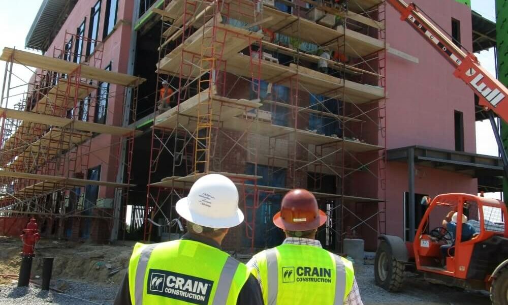 Two construction workers looking at a building that has been wrapped in weather-protecting materials