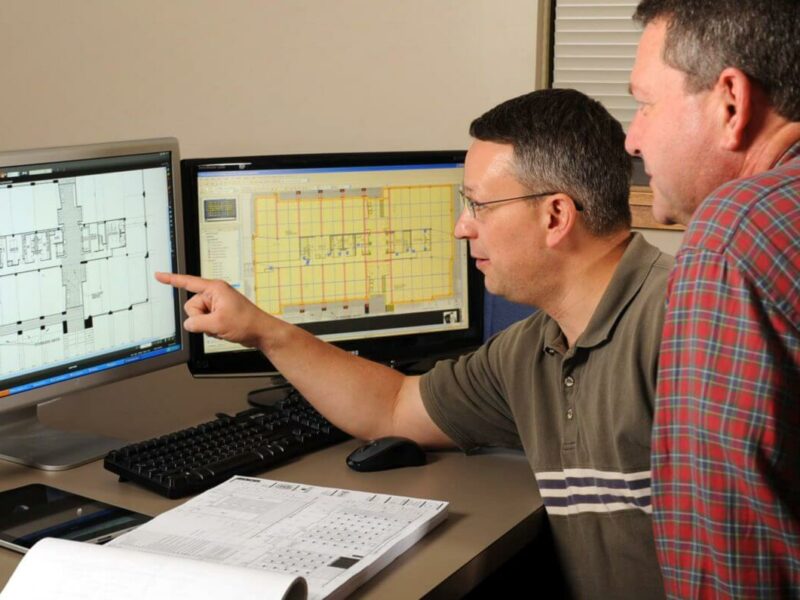 A contractor and an architect discussing a project while pointing at a computer.