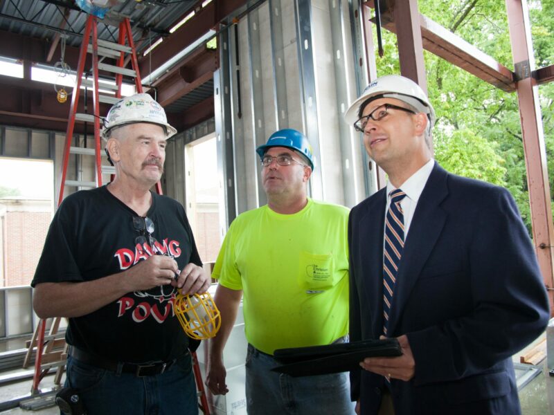 1 project manager with an iPad and 2 construction employees stand together in a construction site