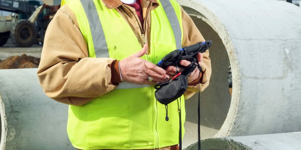 a Crain Construction employee smiling while holding an iPad on a construction site wearing a hard hat and safety vest