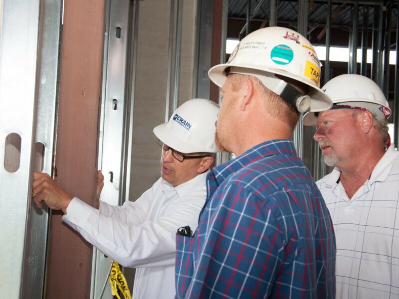 Three construction workers looking at the inside of a framed building with hard hats on.