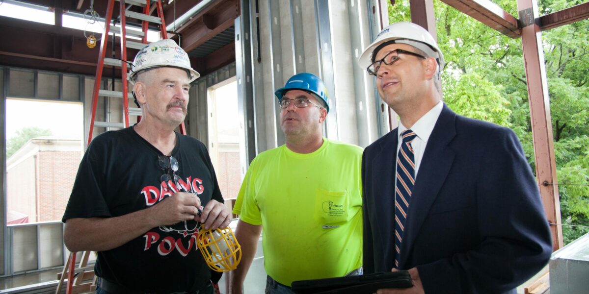 1 project manager with an iPad and 2 construction employees stand together in a construction site