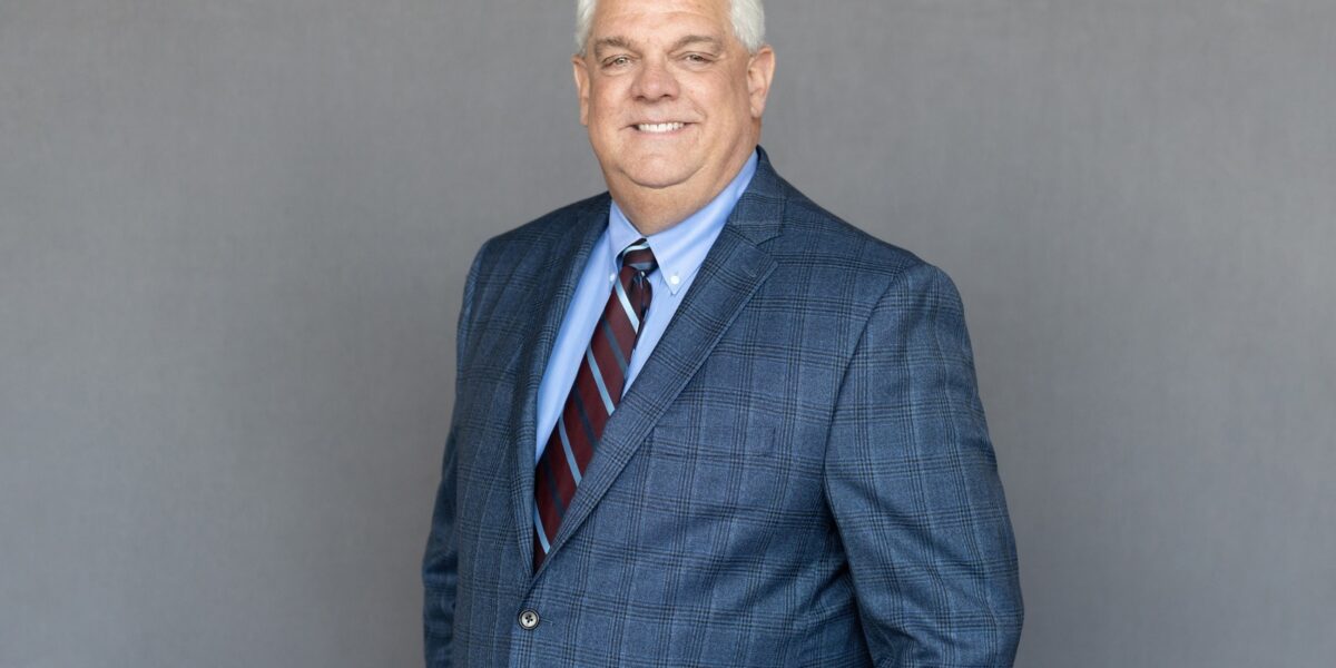 Portrait of Jim Pedigo wearing professional attire, with a friendly smile, in a well-lit indoor setting.