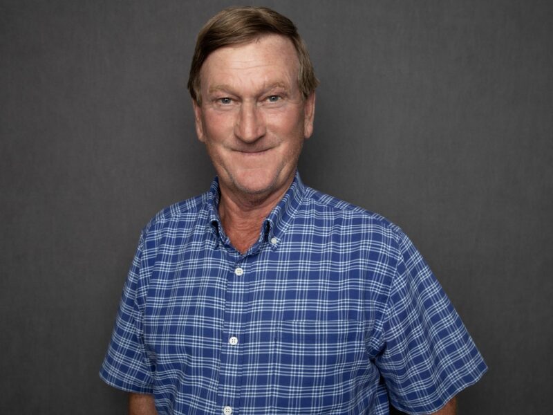 Portrait of JR Howell, a senior superintendent at Crain Construction, in professional attire, smiling and standing against a plain grey background.