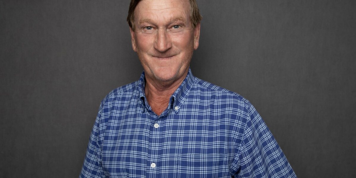 Portrait of JR Howell, a senior superintendent at Crain Construction, in professional attire, smiling and standing against a plain grey background.