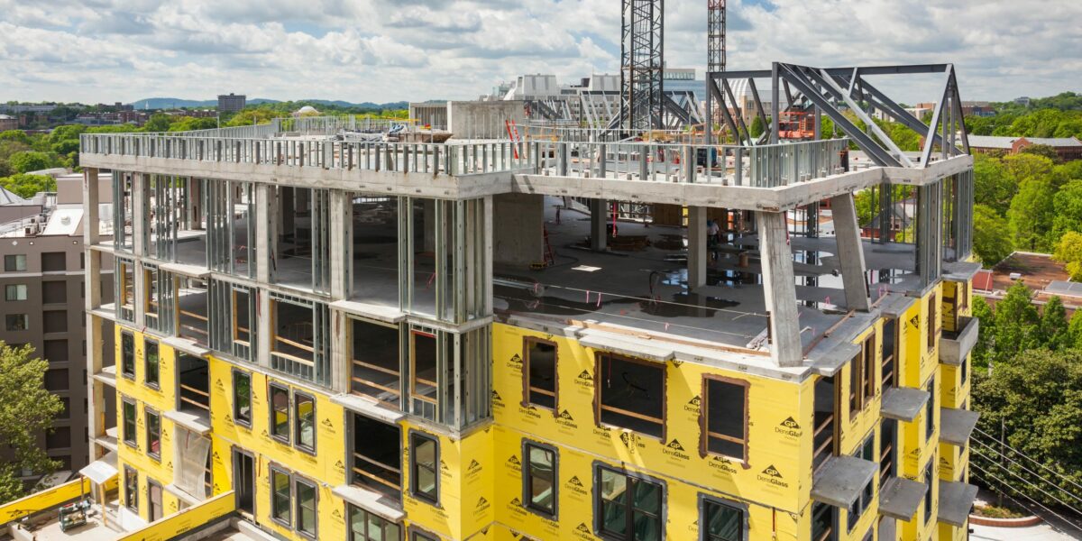 Commercial building under construction with house wrap and metal framing partially complete.