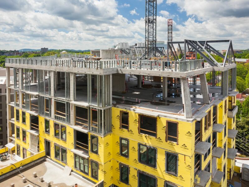 Commercial building under construction with house wrap and metal framing partially complete.