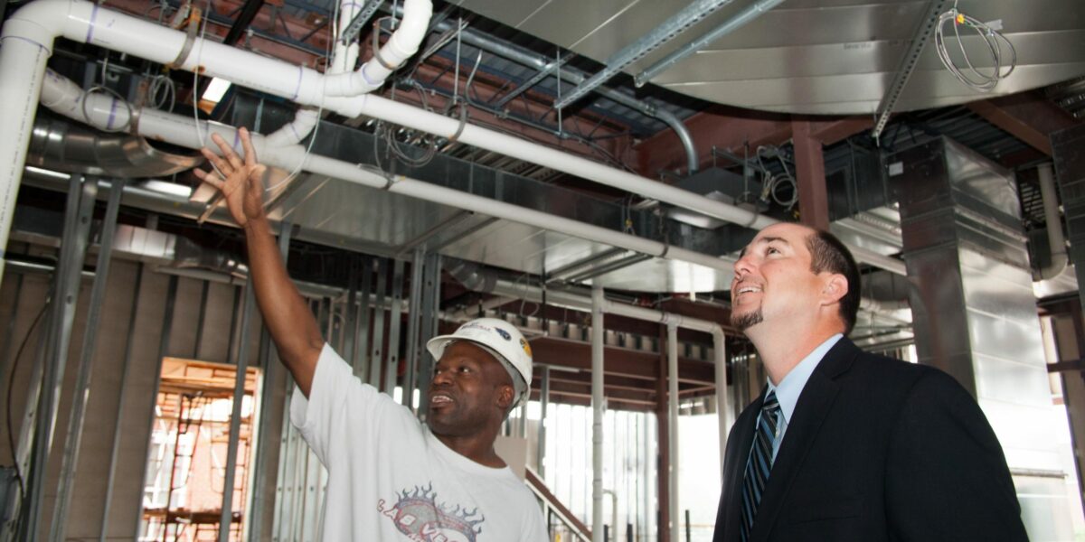 construction worker with hardhat showing project under construction to man in suit