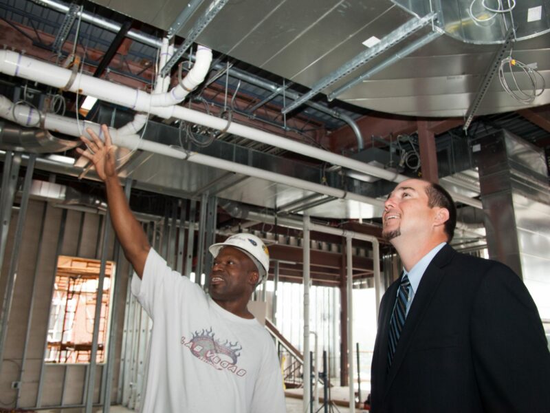 construction worker with hardhat showing project under construction to man in suit