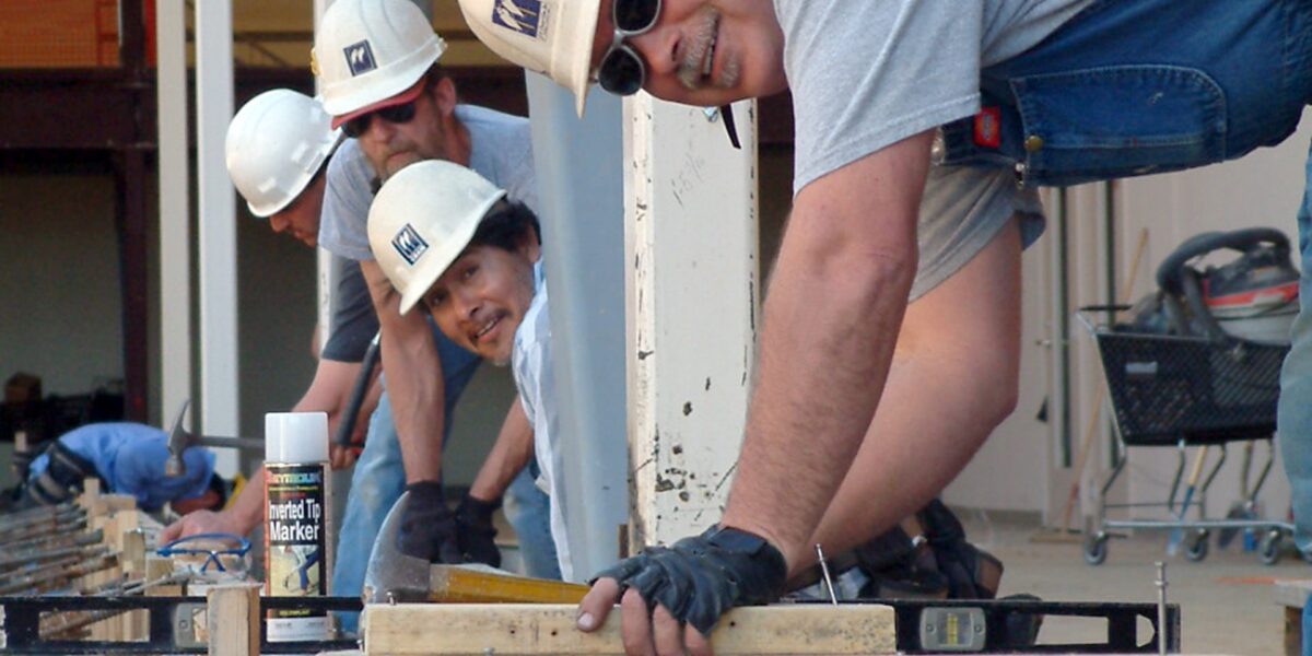 Smiling construction workers standing over beams.